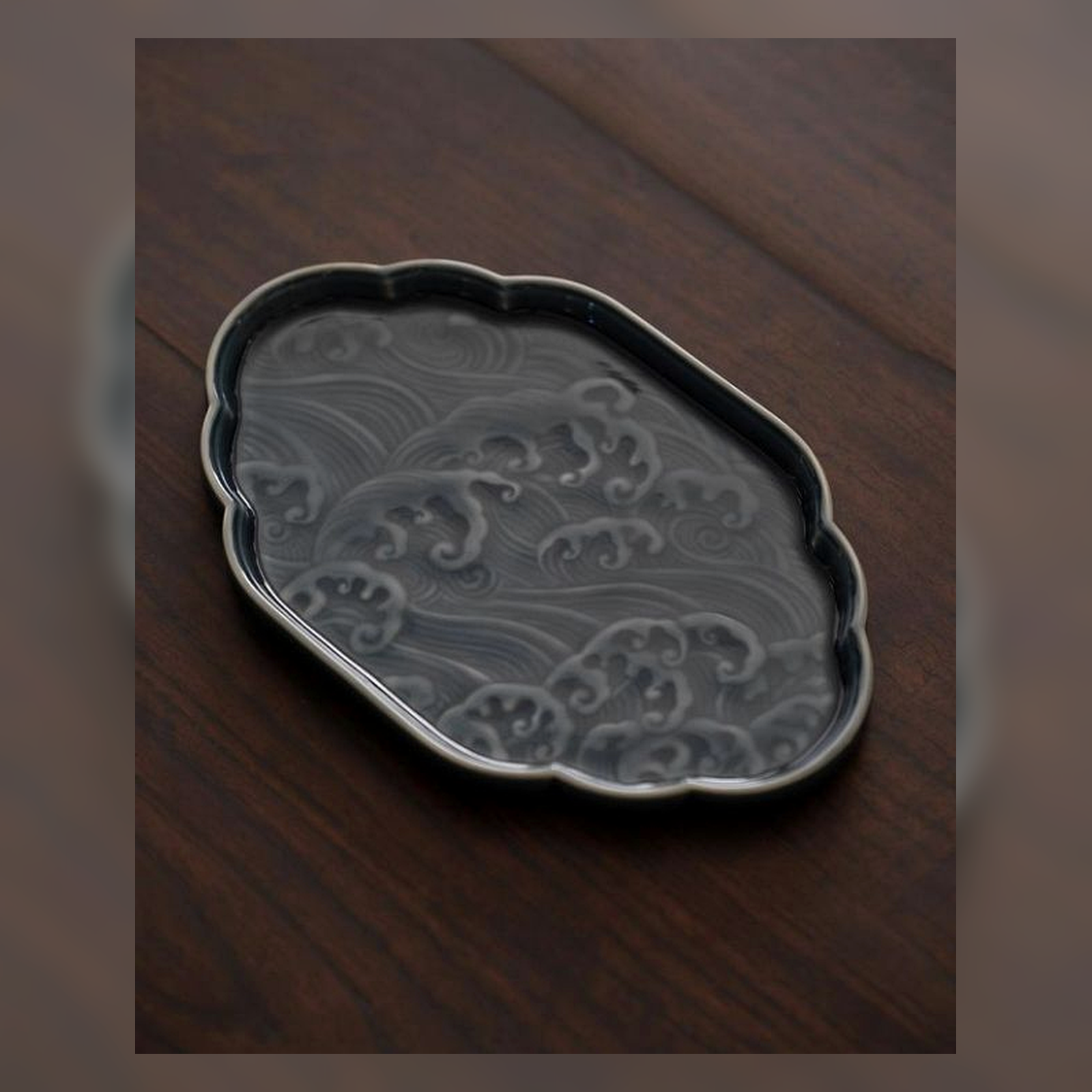Dark ceramic catchall tray with an organic rim on a wooden table.
