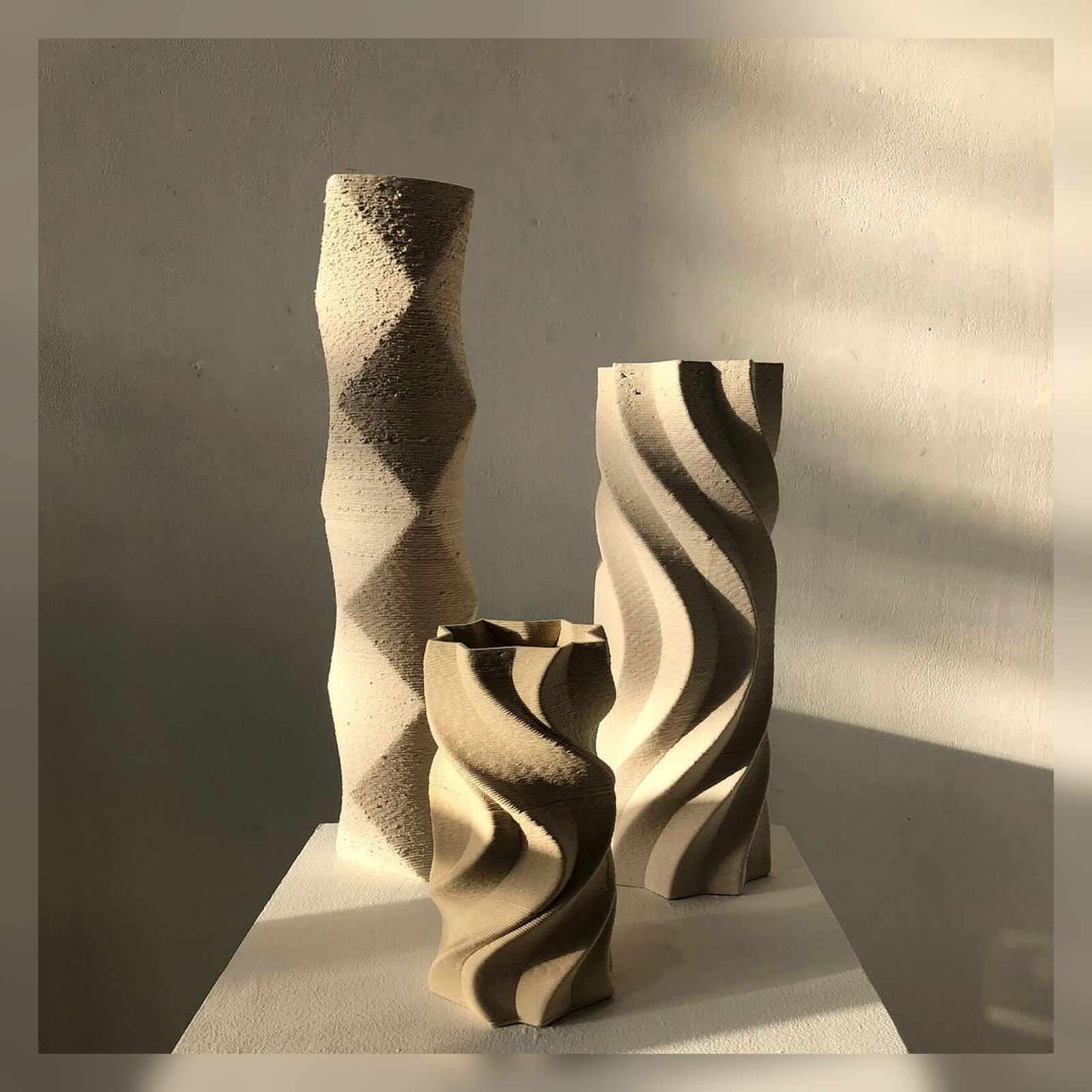 Three sculptural ceramic vases with ribbon-like shadows.