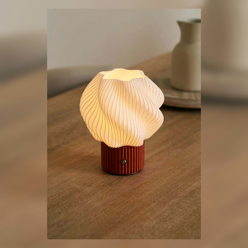 Small shell-like table lamp glowing on a wooden table.